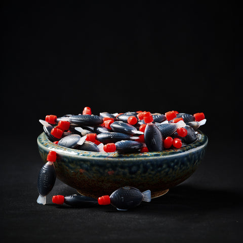 Bowl of individual fish shaped soy sauce sachets on a black background