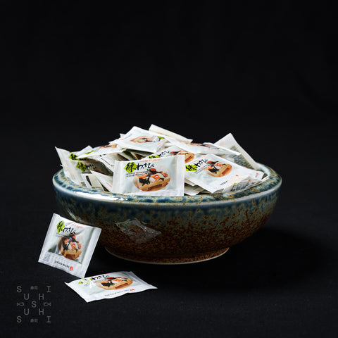 Bowl of individual packets of wasabi on a black background