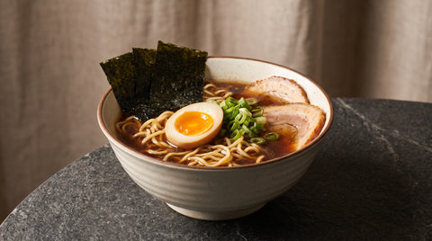 A bowl of ramen noodles with broth, egg and toppings, editorial food photography