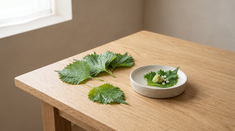 Fresh green shiso leaves beside a small dish, editorial food photography