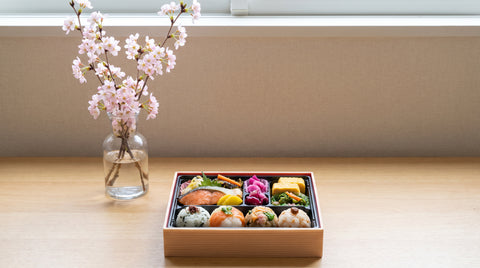 Cherry blossom branches beside a bento box of colourful Japanese dishes
