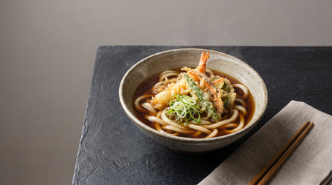 Bowl of udon noodles in broth with tempura and spring onion