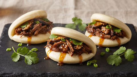 Steamed bao buns filled with savoury filling and glossy sauce, editorial food photography