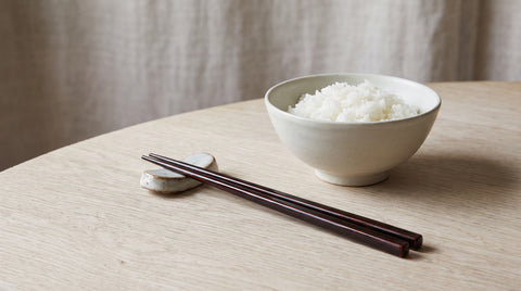 Lacquered Japanese chopsticks on a rest beside a bowl of rice