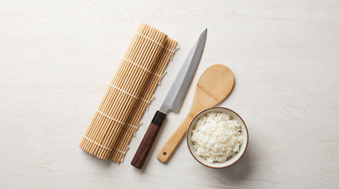 Flat lay of essential sushi-making tools including a bamboo mat and knife