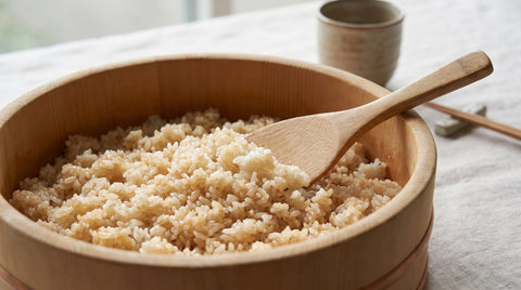 Glossy seasoned sushi rice being fanned in a wooden hangiri bowl