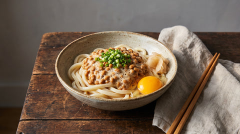 A bowl of udon noodles topped with fermented natto, editorial food photography