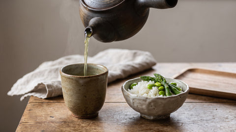Green tea being poured beside a bowl of steamed rice and vegetables