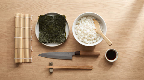 Flat lay of sushi-rolling equipment including a bamboo mat and nori