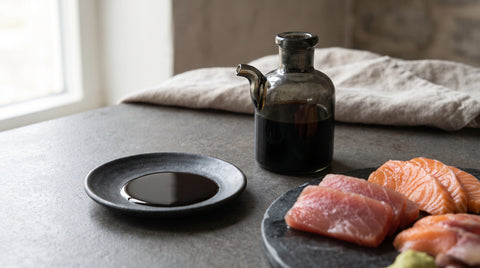 Dish of tamari soy sauce beside sashimi pieces for dipping