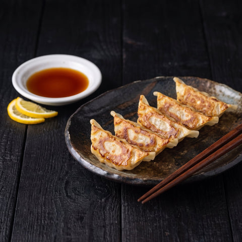 Pan-fried gyoza with a white dish of Kōmi Yuzu Ponzu for dipping, serve view