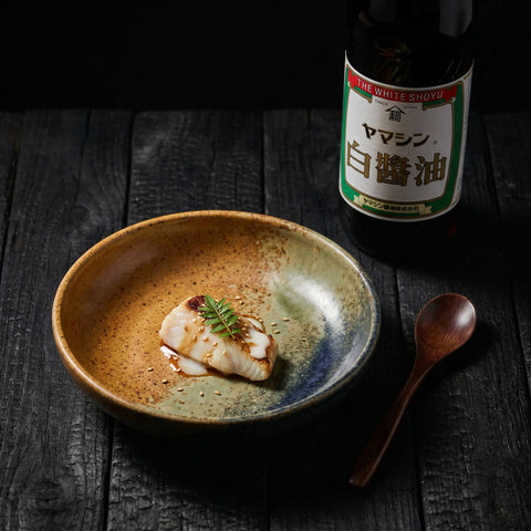 Pale gold white soy sauce poured into a small dish beside the bottle