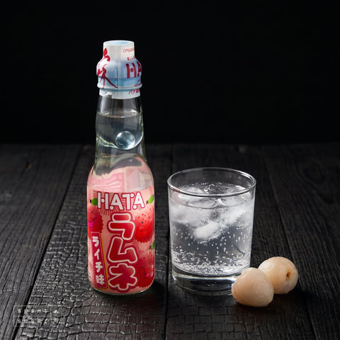 Hata Lychee Ramune 200ml, bottle beside a glass of ramune and fresh lychees