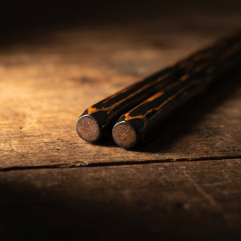 Two wooden chopsticks with tortoiseshell pattern on a wooden surface