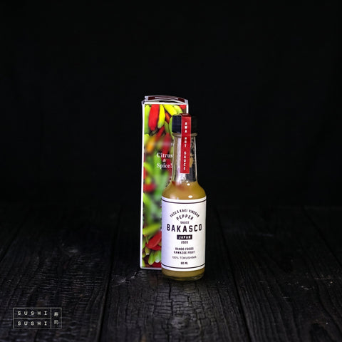 Bakasco Yuzu & Pepper Hotsauce, 60mL, bottle and box on charred wood