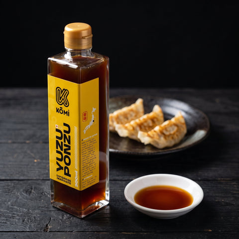 Kōmi Yuzu Ponzu 300ml bottle with gyoza and a dish of ponzu, three-quarter view