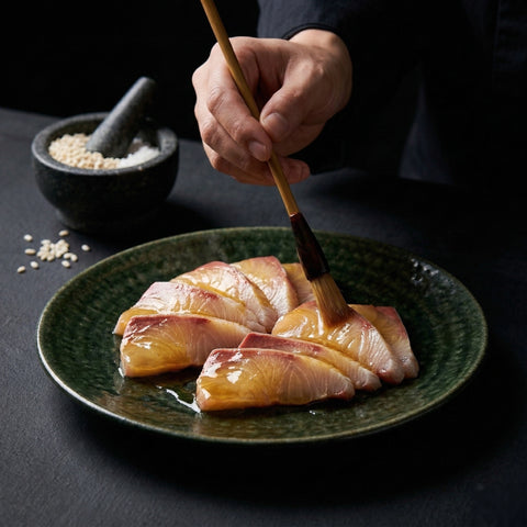 A chef's hand uses a lacquer brush to glaze the fish with clear, golden Liquid Shio Koji