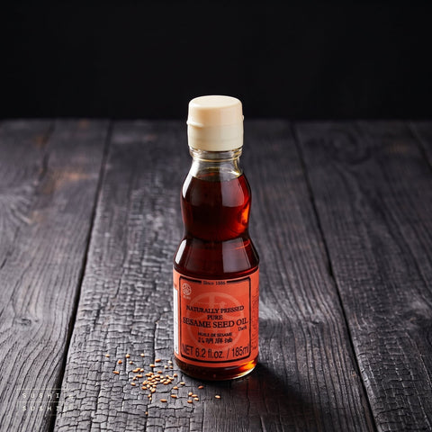 Kuki, Dark Roast Sesame Oil, 170g, bottle on charred shou sugi ban wood against a black backdrop