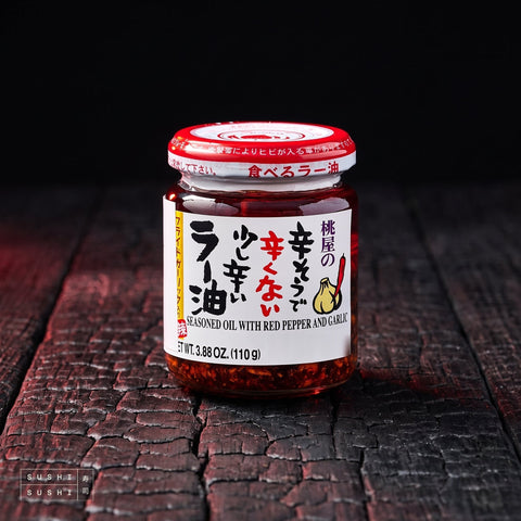 Momoya Crispy Chilli Oil with Fried Garlic (Taberu Rayu) 110g, jar on charred wood