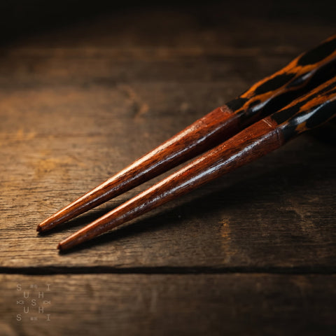 Wooden chopsticks on a dark wooden surface with 'Sushi Sushi' branding.